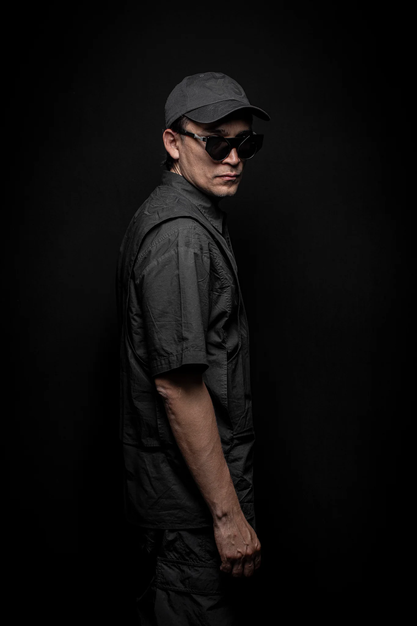 Studio portrait of a creative director wearing black clothing and sunglasses against a black background.
